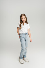 Full length of preteen girl in jeans and t-shirt posing and smiling on grey background.