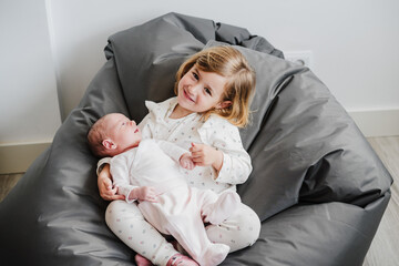 happy big sister toddler holding newborn baby girl at home during daytime.Family and childhood