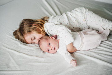 cute big sister toddler kissing newborn baby girl at home during daytime.Family and childhood