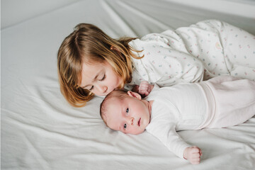 cute big sister toddler kissing newborn baby girl at home during daytime.Family and childhood - 582143687