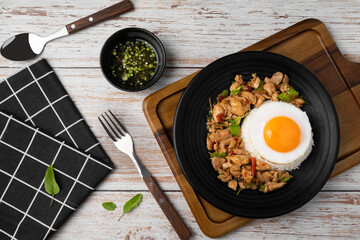 Top view of stir fried basil and chicken on rice with fried egg in black dish on wooden table.