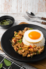 Stir fried basil and chicken on rice with fried egg in black dish on wooden table.