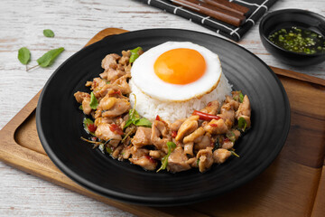 Stir fried basil and chicken on rice with fried egg in black dish on wooden table.