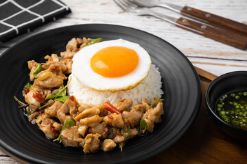 Closeup of stir fried basil and chicken on rice with fried egg in black dish on wooden table.