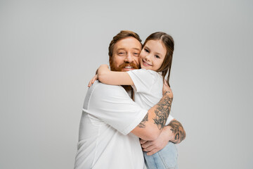 Bearded man hugging carefree daughter and looking at camera isolated on grey.