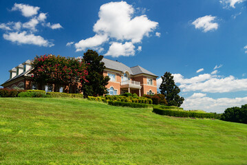 Fototapeta na wymiar Luxurious country house on a hill against a blue sky. Green lawn and landscaping.