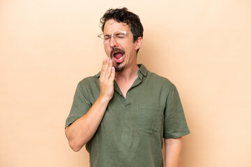 Young caucasian man isolated on beige background yawning and covering wide open mouth with hand