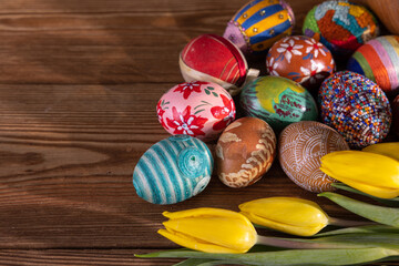 Colorful Easter eggs arranged on brown boards with a few yellow tulips.