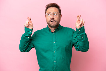 Middle age caucasian man isolated on pink background with fingers crossing and wishing the best