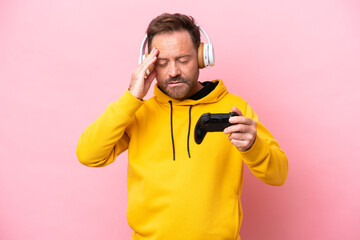 Middle age man playing with a video game controller isolated on pink background with headache © luismolinero