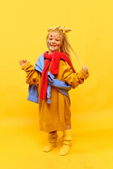 Full-length photo of little girl standing and wearing big clothes, smiling with hands to camera over yellow background