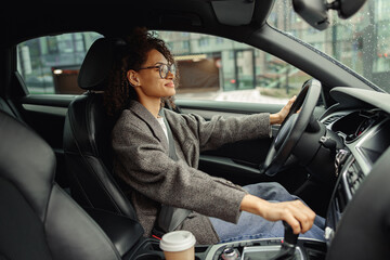 Attractive woman driving car in city with one hand on steering wheel and another on gear lever