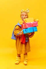 Full-length photo of little girl holding gifts, boxes with surprised face over yellow background. Concept of celebration, ad, children's products, childhood, child model, family