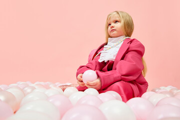 Obraz na płótnie Canvas Photo of little upset girl sitting among balls over pink background. Concept of emotions, childhood, children's games, child model, ad, children's products