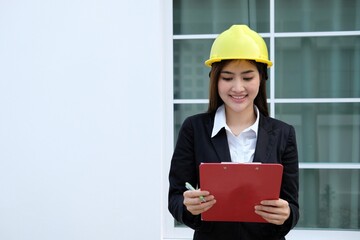 Portrait of a Happy Young Beautiful Female Engineer Wearing yellow Hard Hat, Using Laptop Computer in Office at Car Assembly Plant. Industrial Specialist Working on Vehicle Design in Modern Facility.