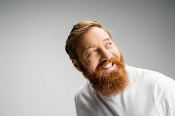Happy and bearded man in t-shirt looking away isolated on grey.