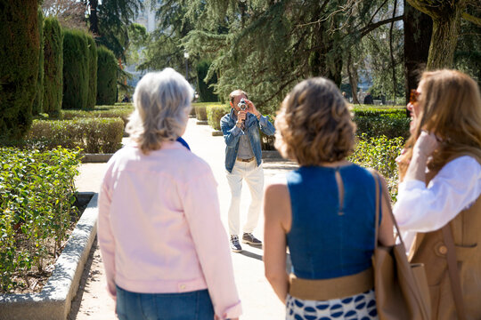 group of middle-aged friends pose in the park while a friend takes pictures of them