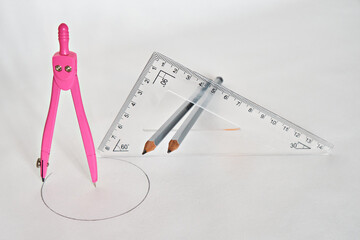 A drawing compass and a triangular ruler with two pencils in the middle of the ruler, on a white...