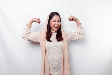 Excited Asian Muslim woman wearing a headscarf showing strong gesture by lifting her arms and...