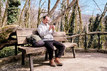 Fototapeta premium Senior asian man uses cell phone on wooden bench in relict forest.