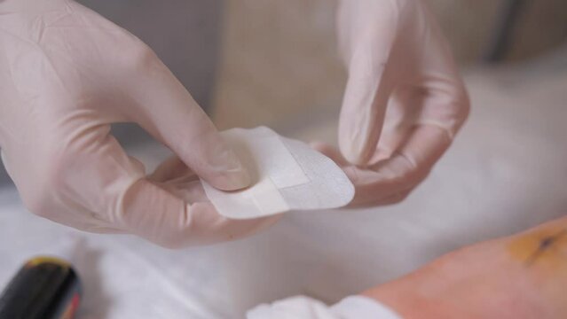 Close-up of a nurse spraying an aerosol of iodine solution on a sterile patch for sealing a postoperative suture.