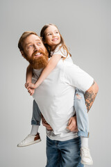 Smiling father holding preteen daughter and looking away isolated on grey.