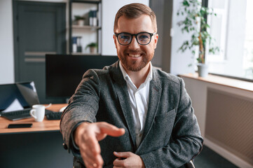 Giving the hand, greetings gesture. Businessman in suit is in the office with computer © standret