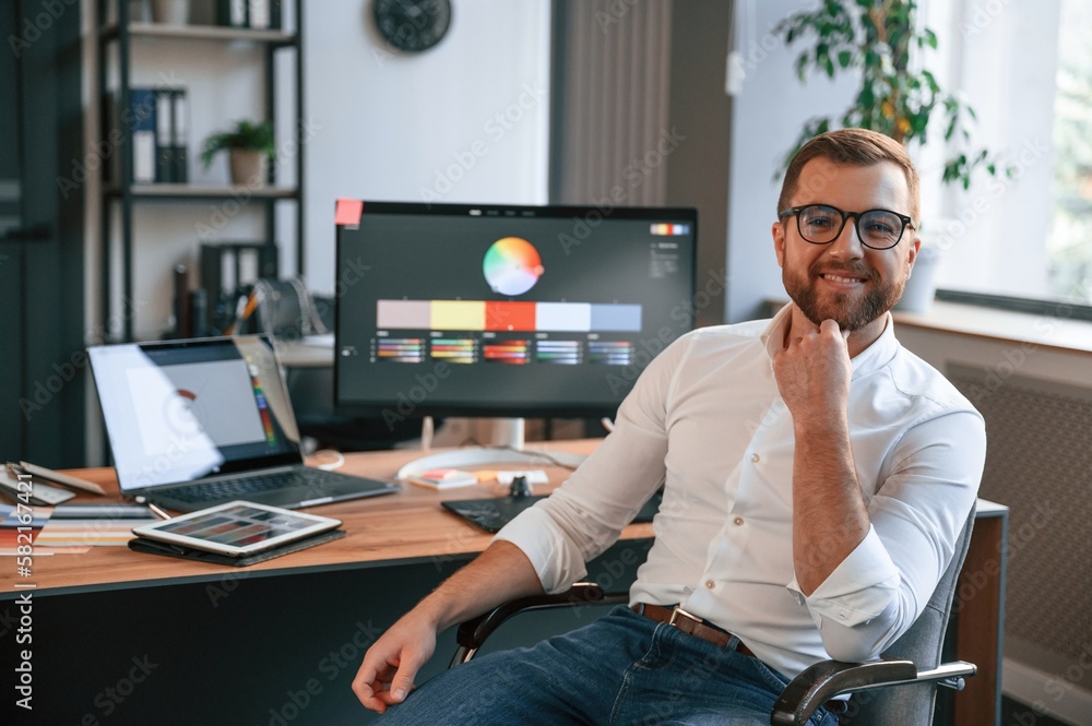 Poster sitting and smiling. man in formal clothes is working in the modern office. using computer