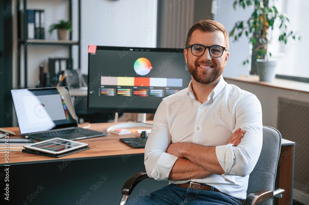 Poster sitting and smiling. man in formal clothes is working in the modern office. using computer