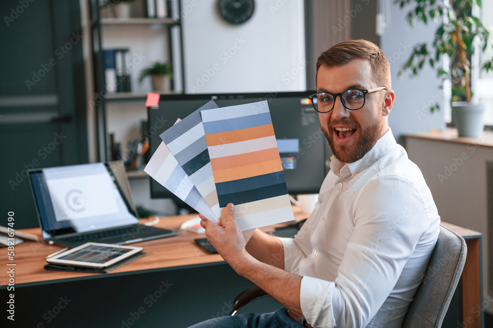 Poster designer is choosing different colors for project. man in formal clothes is working in the modern of