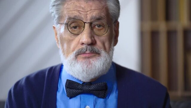 Portrait of an elderly man grandfather teacher with a gray beard in glasses looks at the camera sighs tired feels bad