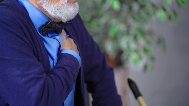 Grandfather, an elderly senior man, sits, clutches his chest, has a heartache, breathes heavily, sighs, close-up
