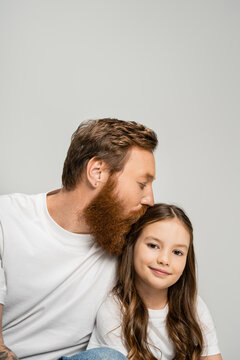 Bearded man in white t-shirt kissing smiling daughter isolated on grey.