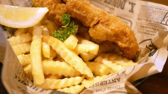 close up view to a plate of fish and chips while using hand pick up french fries from dish for dinner lunch meal