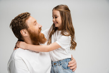 Smiling preteen girl hugging bearded dad isolated on grey.