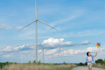 Progressive young asian boy playing with wind pinwheel toy in the wind turbine farm, green field...