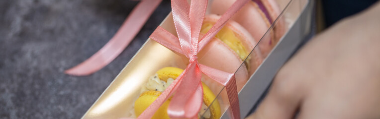 a woman confectioner is tying a box of macarons cookies with a pink ribbon. hands close up. home bakery concept.