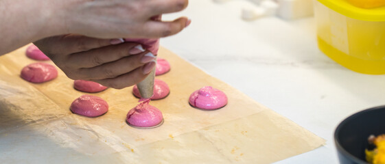 Obraz na płótnie Canvas the confectioner squeezes out drops of pink macarons dough. close-up. home bakery concept.