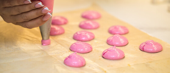 Obraz na płótnie Canvas the confectioner squeezes out drops of pink macarons dough. close-up. home bakery concept.