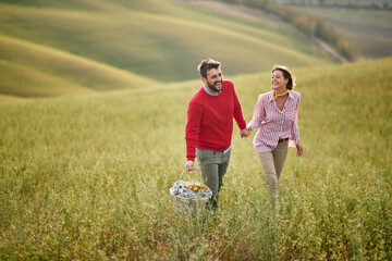 A young cheerful couple is excited about a picnic they will have on a large meadow. Love, relationship, together, nature