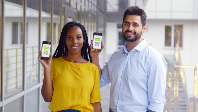 Multiethnic couple looking at camera showing vaccinated qr-code on cellphone