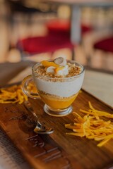 Vertical closeup of a glass of dessert with mango yogurt on a wooden board with mango slices