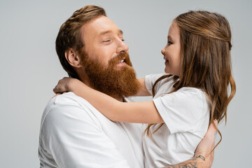 Bearded man hugging cheerful preteen child isolated on grey.