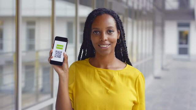 Portrait of smiling African-American woman holding smartphone with vaccinated covid-19 certificate on display