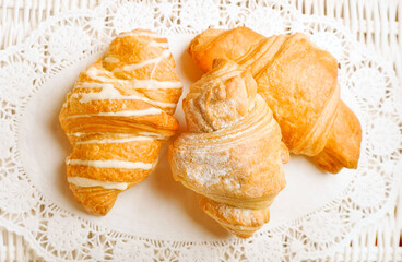 Three baked french croissants lying on festive white lace table-cloth in rustic style 