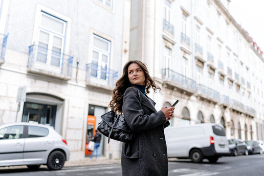 Calm woman browsing smartphone and looking away on street