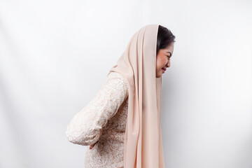 Tired upset young Asian Muslim woman wears headscarf suffering from pain, muscle spasm at...
