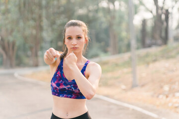 A beautiful sportswoman in sportswear is performing boxing exercises outdoors in an Autumn city park background.