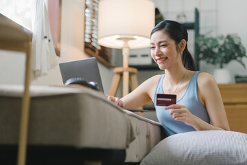 A happy young woman is shown shopping online using her laptop and credit card at home.