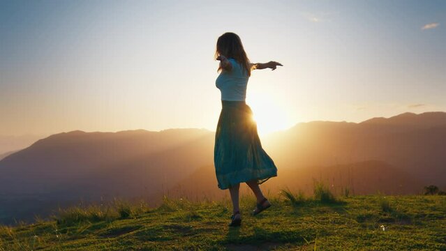 Young woman dances on the hill at sunrise. Woman enjoys sunrise and dances